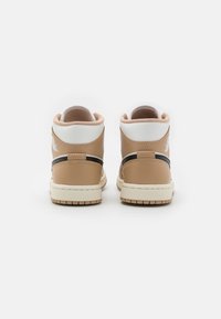 Ett par beige och vita högklackade sneakers med svarta randdetaljer, sedd från baksidan mot en helt vit bakgrund.