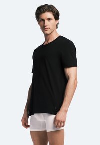 Black short-sleeve T-shirt made of soft cotton, featuring a crew neck. Worn over white fitted boxer shorts. Plain design, no patterns.