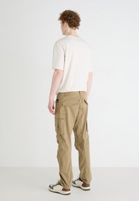 Beige katoenen t-shirt gecombineerd met khaki cargobroek met meerdere zakken en een relaxte pasvorm, gedragen met wit en bruine sneakers.