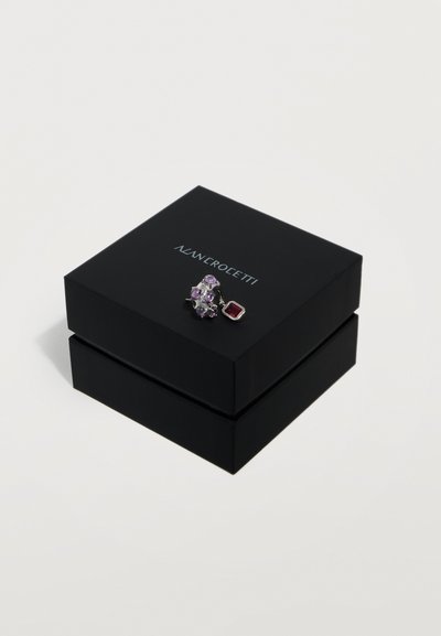 Crna kutija za nakit sa srebrnim logom "ALAN CROLETTI", na vrhu srebrni prsten s ljubičastim i crvenim dragim kamenjem.