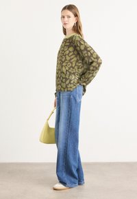 Olijfgroen gebloemd langemouwen top met een witte streep, gecombineerd met hoge taille blauwe wijde jeans en een lichtgroene schoudertas.