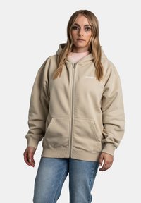 Beige zip-up hoodie met een voorzak, ribgebreide manchetten en zoom. Bevat een capuchon en het "PEGADON" logo in het wit op de linkerborst.