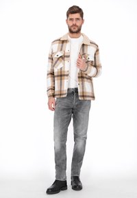 Chaqueta de franela a cuadros marrón y blanca con cuello suave, dos bolsillos en el pecho, usada sobre una camiseta blanca y jeans grises, combinada con botas negras.