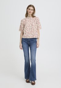 Haut à manches courtes fleuri en crème avec des fleurs rouges et vertes, associé à un jean bleu évasé et des ballerines marron. Design simple et décontracté.