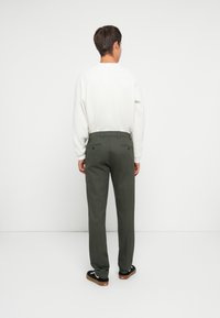 Olive green trousers with a tailored fit, featuring a flat front, two back pockets, and subtle textured fabric. Worn with a white sweater and sneakers.