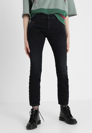 Jean noir slim porté avec des bottines noires à lacets et des chaussettes résilles, associé à un sweat-shirt court vert avec cordons.