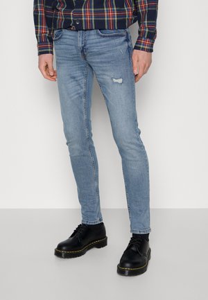 Ljusblå skinny jeans med urtvättade områden och ett hål på knät, samsas med svarta snörskor med gula sömmar.
