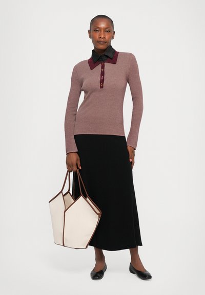 Woman wearing a mauve long-sleeve top with black collar and buttons, black midi skirt, black flats, holding a large beige and brown tote bag.