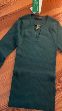 Top de manga longa verde com nervuras, decote em V e um detalhe decorativo de corrente prateada. Etiqueta com a inscrição "Ecovero" anexada.