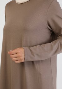 Langärmliges, taupefarbenes Kleid aus glattem Stoff, mit einem lockeren Schnitt, einem runden Ausschnitt und dezenten Nähten an den Manschetten.