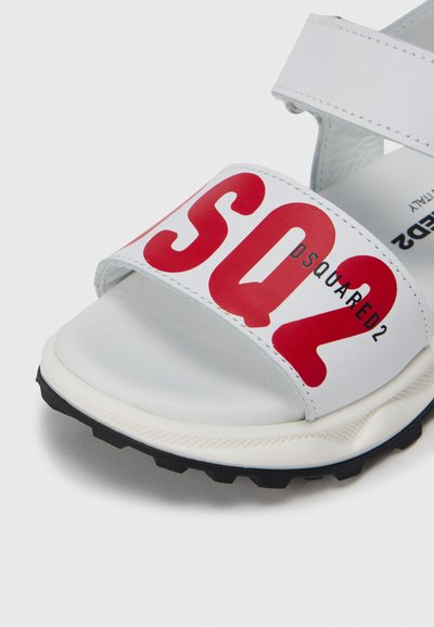 Sandales blanches avec une sangle large présentant le texte rouge "SQ2" en grand et le logo "DSQUARED2". Semelle texturée offrant une bonne adhérence.