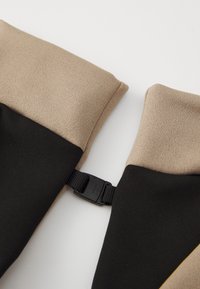Stretch-stoff med beige og svarte fargeblokker, med en svart plastspenne for sikker festing. Glatt tekstur med en tettsittende design.