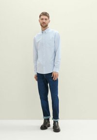 Camisa azul claro de botones con un bolsillo, combinada con jeans azul oscuro y botines negros. La camisa presenta un sutil patrón a rayas.