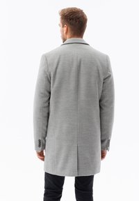 Cappotto grigio in misto lana con colletto classico, spacco posteriore singolo e dettaglio a tre bottoni sui polsini. Vestibilità su misura, lunghezza media.