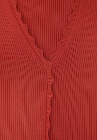 Rood geribd breiselstof met geschulpte randen langs een V-vormige halslijn, met gedetailleerde textuur en stiksels.