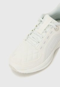 Sneaker bianco con texture trapuntata, tessuto liscio, accenti di design sottili e lacci grigio chiaro. Caratterizzata da una punta arrotondata e un dettaglio del logo.