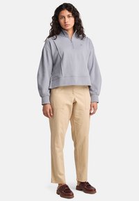 Ljusgrå croppad pullover med dragkedja i halsen, ribbat nederkant och avslappnad passform; parat med beige cargobyxor och bruna snörskor.