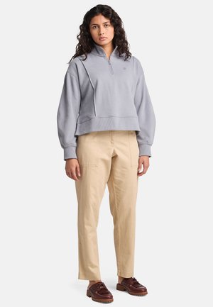 Pull léger gris clair à col zippé, avec un ourlet côtelé et une coupe décontractée ; associé à un pantalon cargo beige et des chaussures à lacets marron.
