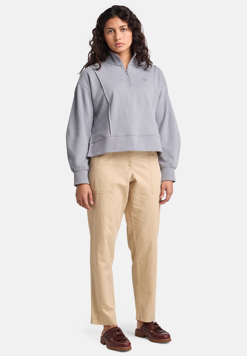 Ljusgrå croppad pullover med dragkedja i halsen, ribbat nederkant och avslappnad passform; parat med beige cargobyxor och bruna snörskor.