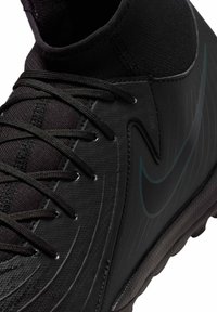 Scarpa sportiva nera con una superficie texturizzata, vestibilità stretta e design curvato. Presenta lacci prominenti e un sottile logo Nike in una tonalità più scura.