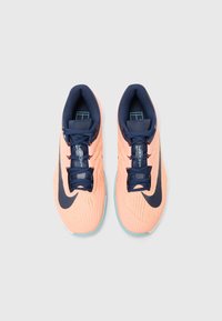 Nike bėgimo bateliai, kurių spalvų schema yra persikų ir tamsiai mėlyna, tinklinė viršutinė dalis, briaunoti tekstūros ir kontrastingos tamsios detalės ant swoosh ir raiščių.