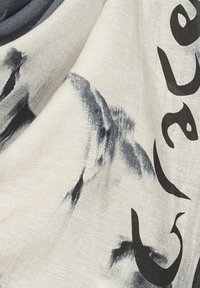 Sciarpa leggera con una texture morbida, caratterizzata da un colore di base crema, una stampa astratta nera e dettagli di testo grafico.