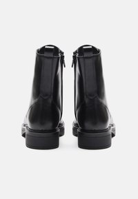 Botas de tobillo de cuero negro con un acabado suave, que presentan cremalleras en la parte trasera, tacones apilados y un diseño limpio y estructurado.