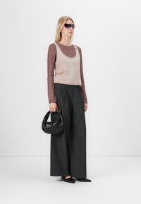 Beige avkortet tanktop over en brun langermet topp, kombinert med svarte brede bukser med pinstriper. En svart veske og solbriller fullfører antrekket.