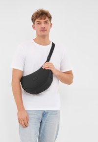 Borsa a tracolla nera realizzata in tessuto testurizzato, forma curvata, con tracolla regolabile e dettaglio del logo sulla parte frontale.