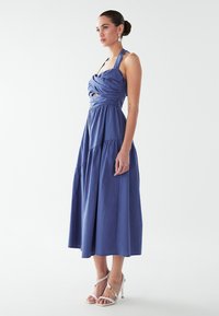 Modra obleka do kolen z zvitim korzetom, okroglim hrbtnim izrezom in večplastno krilom, narejena iz lahkega materiala. Pete so bele.