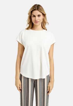 Weißes T-Shirt mit kurzen Ärmeln und rundem Ausschnitt, kombiniert mit gemusterten schwarz-weißen High-Waist-Hosen.