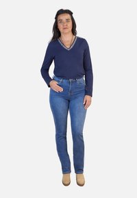 Sudadera de color marino de manga larga con escote en V y acentos metálicos, combinada con unos jeans azules ajustados y botas de tobillo beige. Diseño simple y clásico.