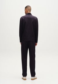 Chándal atlético en color navy con parte superior con cuello y cremallera de cuarto y pantalones a juego. Fabricado con un material suave y de corte relajado.