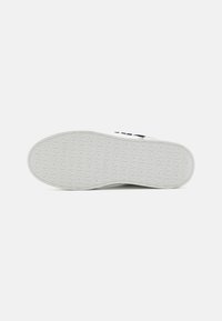 Sole di sneaker bianca con un motivo testurizzato. Presenta un marchio in rilievo. Bordi puliti e lisci con una leggera curvatura. Il materiale sembra resistente.