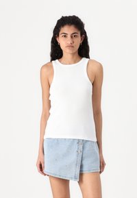 White ribbed tank top with a rounded neckline and sleeveless design, paired with a light blue denim mini skirt featuring studded accents.