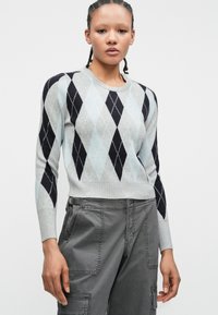 Pull en argyle gris et bleu clair avec des manches longues et un col rond, associé à un pantalon cargo gris. Texture en tricot douce.