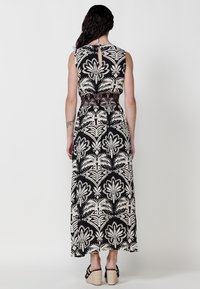 Robe maxi avec un motif floral noir et crème, sans manches, taille cintrée avec un détail élastique, et légère ouverture en forme de clé au dos.