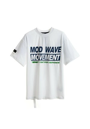 Joven de pie vistiendo una camiseta blanca con la inscripción "MOD WAVE MOVEMENT", pantalones cortos de mezclilla azul, calcetines blancos con estampado y zapatos beige texturizados.