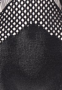 Μαύρο ύφασμα που διαθέτει ένα υφασμένο σχέδιο ανοικτού πλέγματος στην κορυφή και ένα πιο λείο, συμπαγές ύφασμα παρακάτω, αναδεικνύοντας την αντίθεση υλικού και σχεδίου.