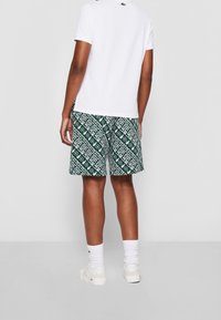 Valkoinen lyhythihainen polo-paita, joka on yhdistetty vihreisiin shortseihin, joissa on valkoinen geometrinen logokuviopainatus. Asusteena valkoiset sukat ja lenkkitossut.