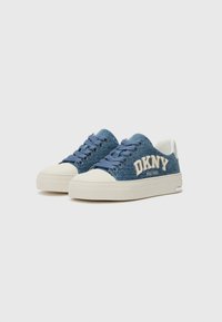 Baskets en denim bleu avec une semelle en caoutchouc crème, ornées d'un logo blanc en relief et de lacets bleus. Texture lisse avec un accent de talon contrastant.