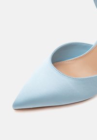 Chaussure femme bleu clair à bout pointu avec une finition satinée lisse et une doublure intérieure beige sur fond blanc.