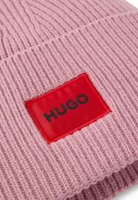 Beanie a coste rosa con una toppa quadrata rossa con il marchio nero "HUGO". Materiale testurizzato con design a risvolto.