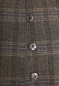 Gros plan sur un tissu à carreaux marron et bleu avec une rangée verticale de trois boutons-pression ronds en métal noir.