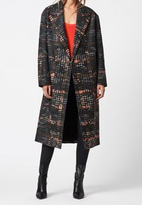 Schwarzer und mehrfarbiger kariertes Wollmantel mit einem doppelt-knöpfbaren Design, großen, eingekerbten Revers und Seitentaschen, getragen über einem roten Oberteil.