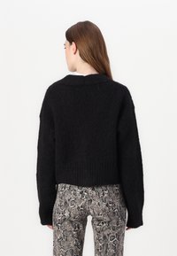 Maglione corto lavorato a maglia nera con finitura testurizzata, caratterizzato da maniche lunghe e un ampio scollo, abbinato a pantaloni aderenti con motivo a serpente.