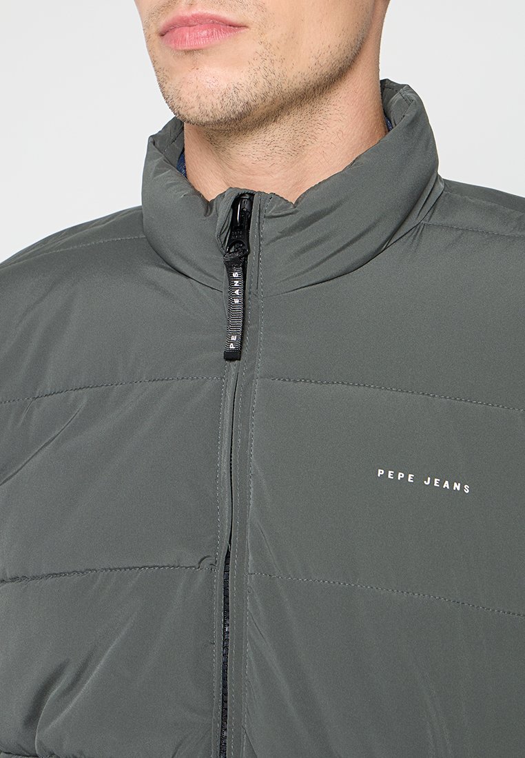Chaqueta acolchada gris con cuello alto, cremallera frontal y paneles cosidos. Presenta el logo de "Pepe Jeans" en blanco en la parte izquierda del pecho.