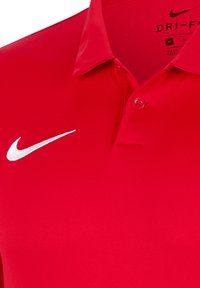 Rotes Polohemd aus Dri-FIT-Gewebe, mit einer Zwei-Knopf-Leiste, weichem Material und einem weißen Nike-Logo auf der linken Brust.
