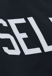 Schwarzer Stoff mit großen, weißen, gestickten Buchstaben, die "SELL" buchstabieren, mit einer strukturierten Oberfläche und sauberen Kanten.