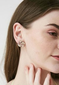 Orecchini a perno color oro con design circolare, caratterizzati da un mix di pietre rosa e trasparenti incastonate su una superficie testurizzata.